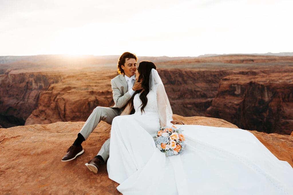 Groom cradles bride's face as he leans in for a kiss with the sunset over Horseshoe Bend behind them