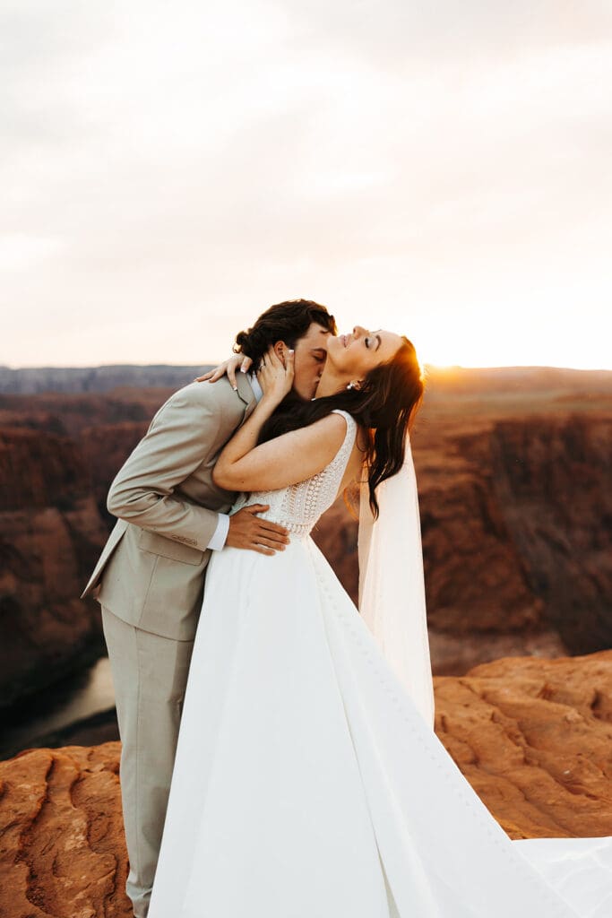 Groom kisses bride's neck as she tips her head back towards the Arizona sun descending over the cliffs of Horseshoe Bend