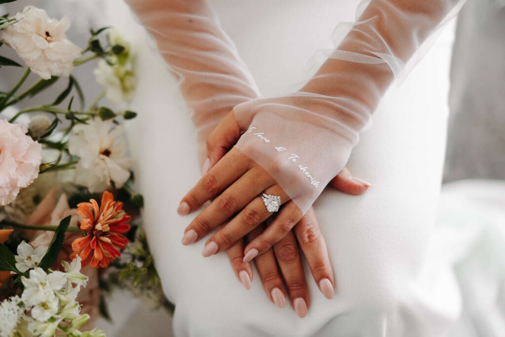 Bride crosses her hands over her lap to showcase her vow=embroidered gloves