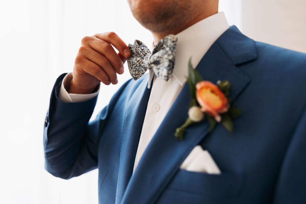 Groom wearing navy blue suit and orange boutounniere fixes his spunky bowtie