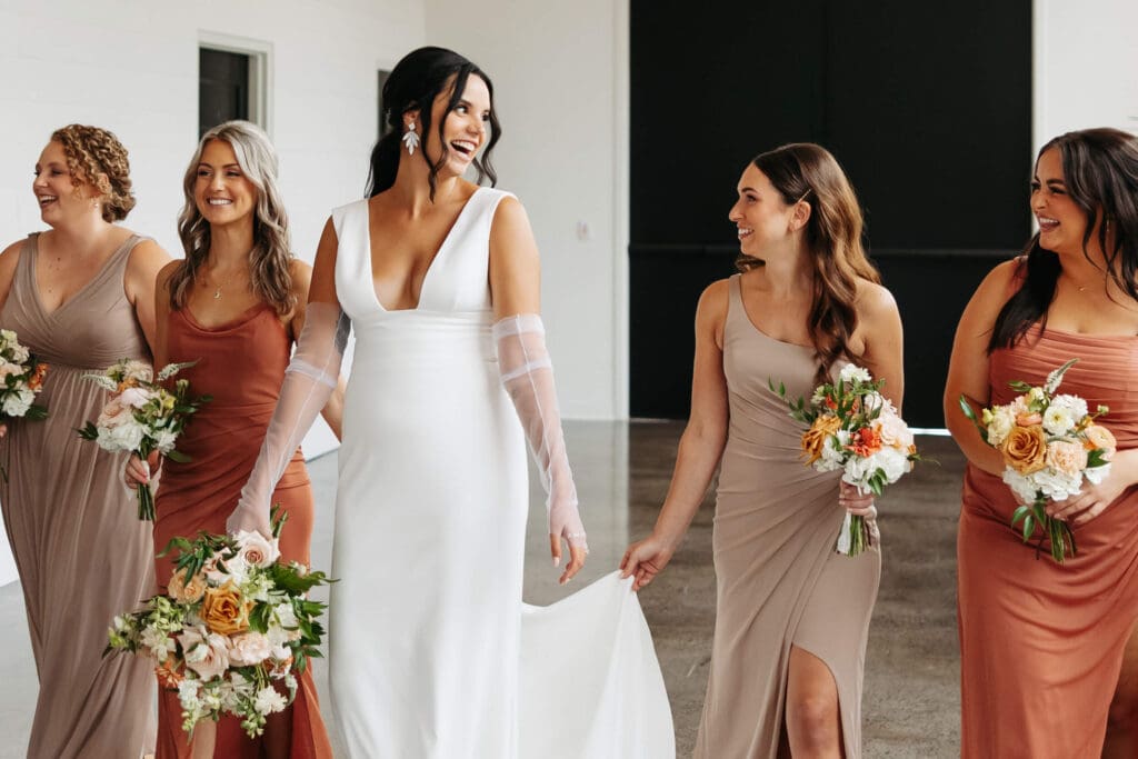 Bride and bridesmaids wearing beige and orange walk in minimalist, sunlight space of Urban Daisy
