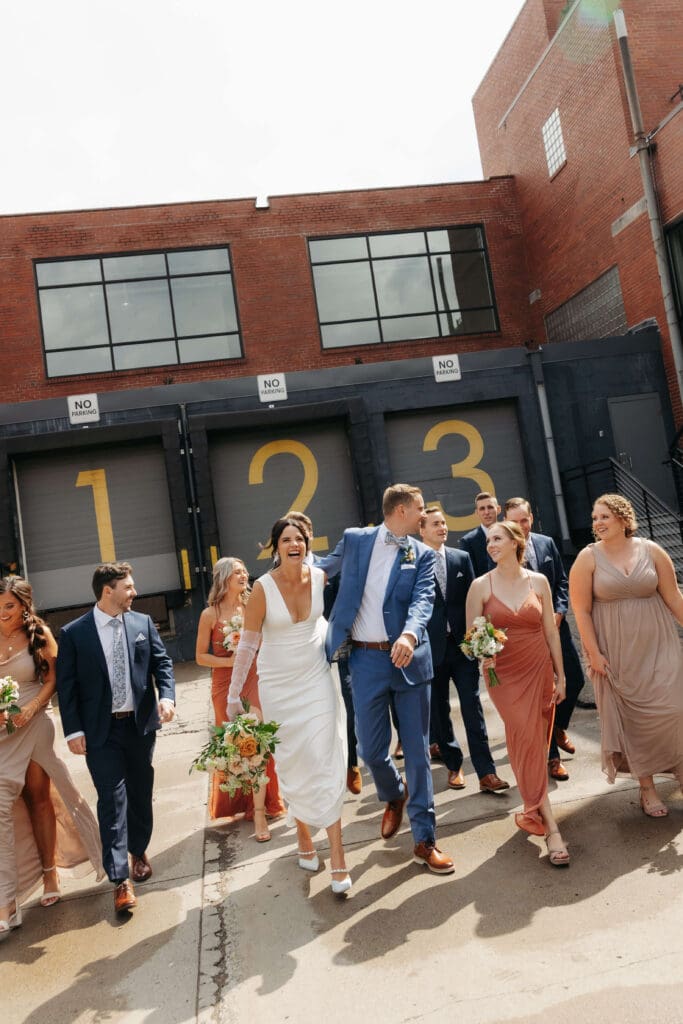 Bridal party and newlyweds laughing and walking outside garage doors of Urban Daisy in downtown Minneapolis