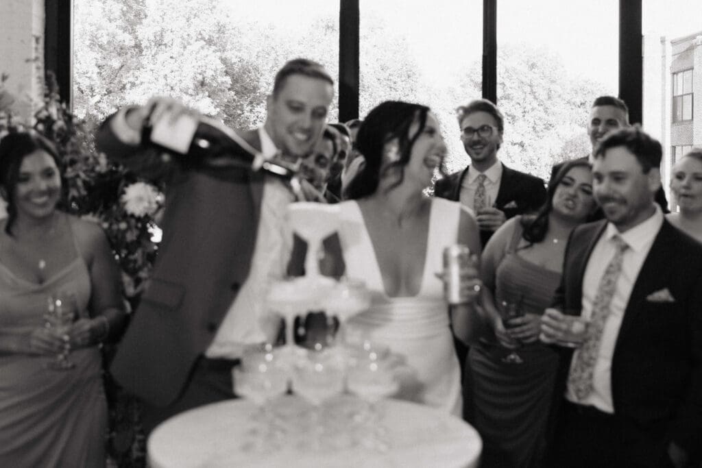 Groom pours champagne tower while bride laughs 