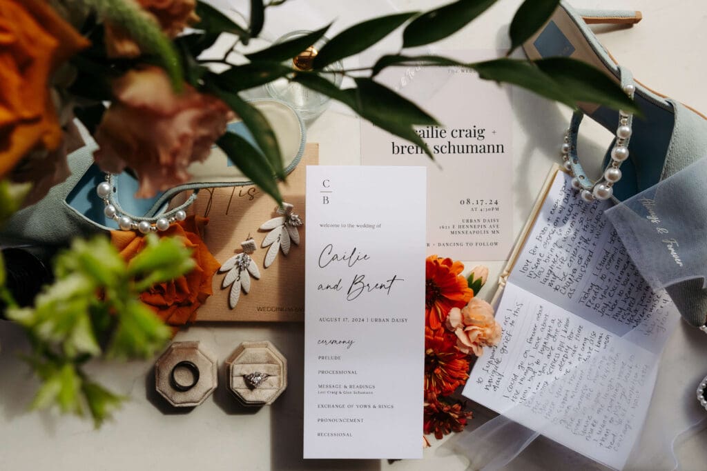 Flatlay details of wedding day including invitations, vowbooks, rings, and pops of floral color