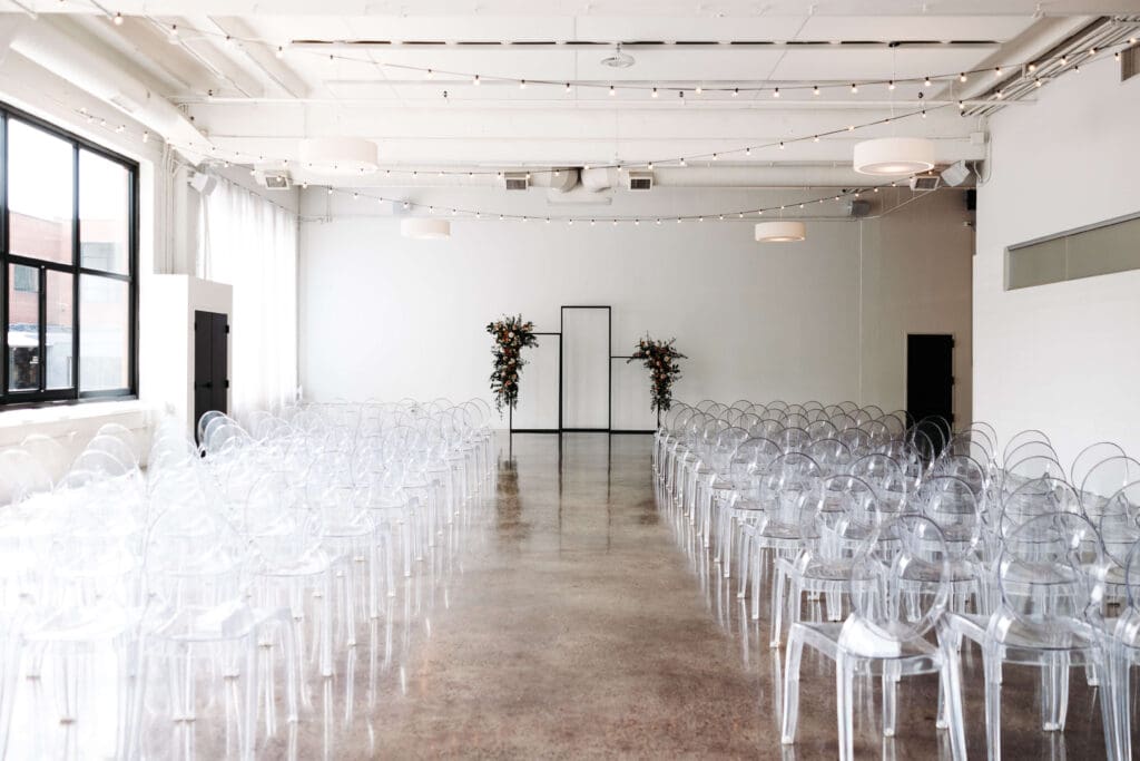 Wide shot of the ceremony space at Urban Daisy with tall windows, clean white walls, and a minimal floral arch.