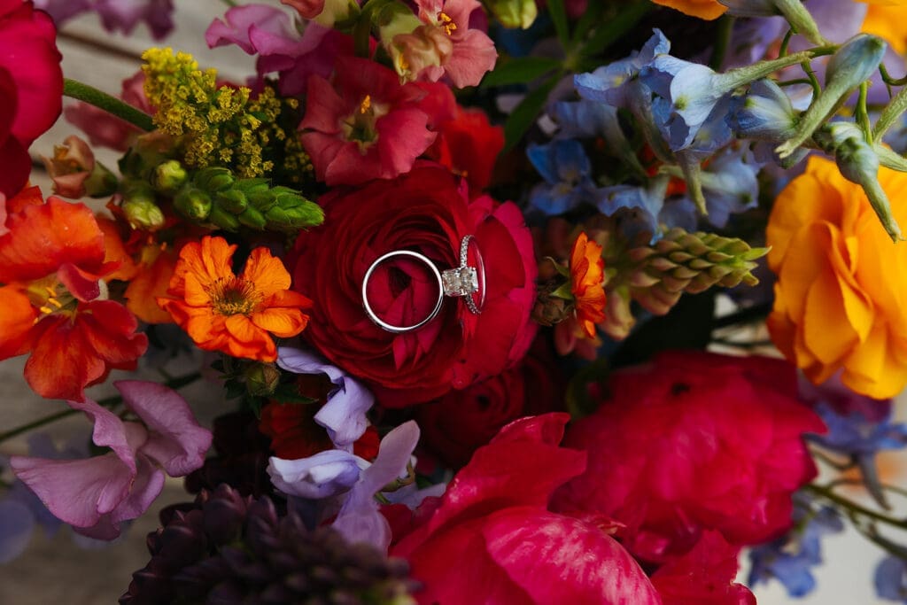 Diamond engagement ring nestled among vibrant garden roses, ranunculus, and colorful wedding florals.