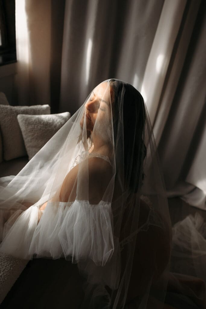 Bride wrapped in a veil during a bridal boudoir portrait, creating an ethereal and artistic wedding-day image.