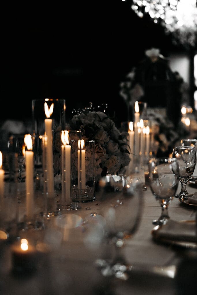 Candlelit wedding reception centerpiece with layered glass hurricanes and romantic floral arrangements after dark.