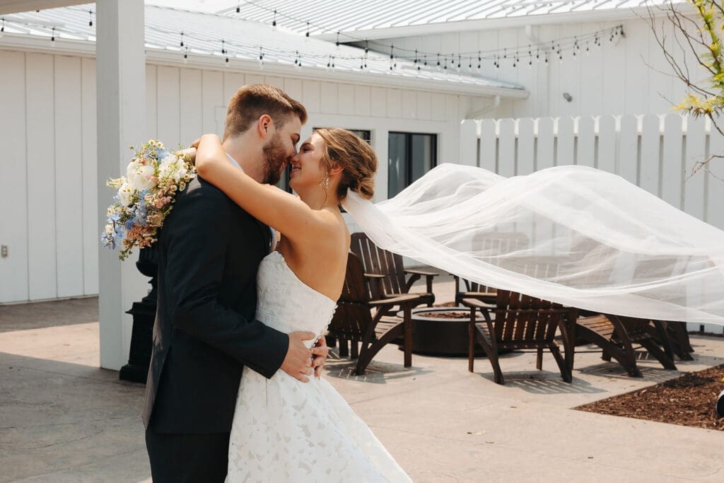 Bride and groom embracing with a flowing veil outside Equestria West at Bavaria Downs, a modern blank canvas wedding venue in Minnesota.