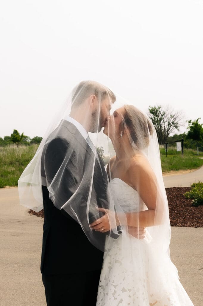 Bride and groom sharing a kiss beneath the veil after their ceremony at one of the most beautiful Minnesota wedding venues.
