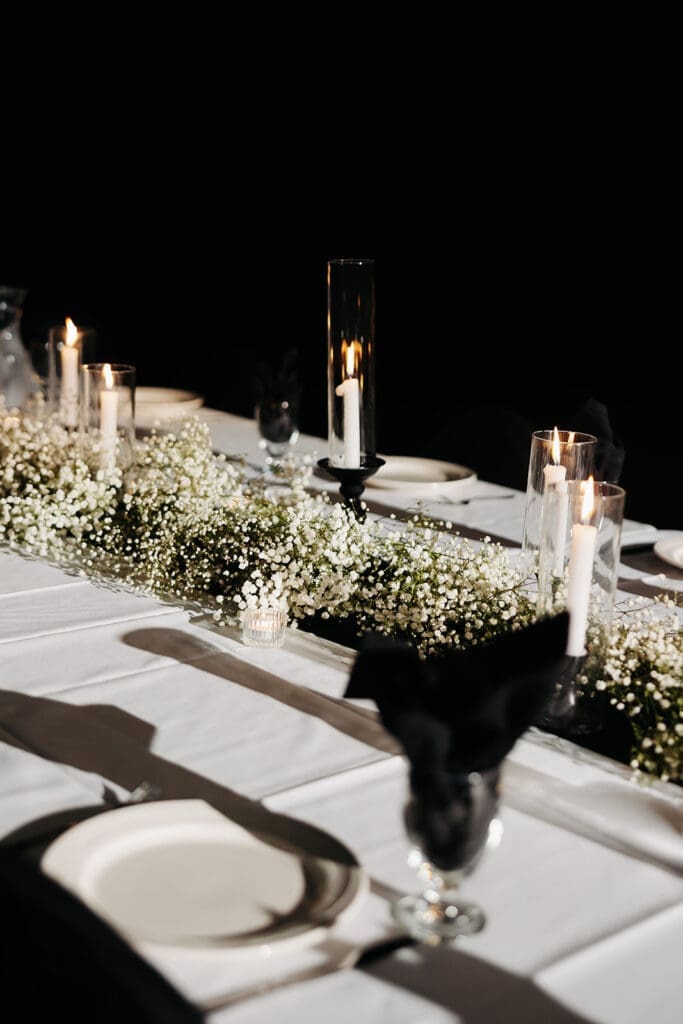 Long reception table lined with baby's breath, taper candles, and elegant place settings under dramatic evening light.