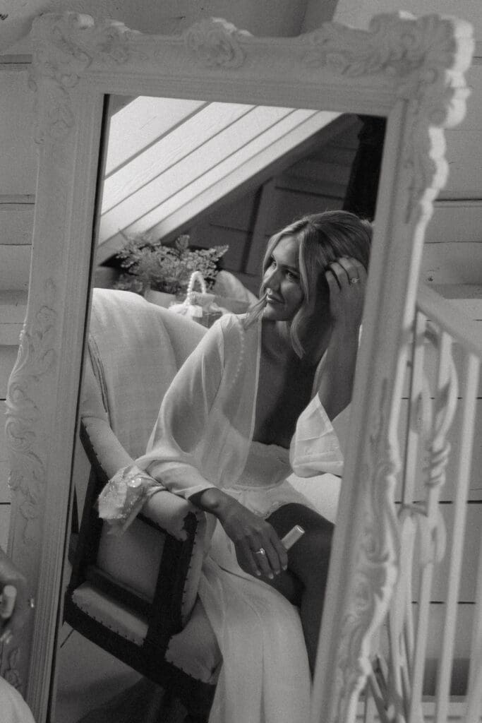 Bride sitting in front of an antique mirror with her veil draped around her while getting ready on her wedding morning.