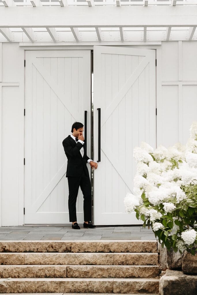 Groom walks outside the double doors at Redeemed Farm in Minnesota moments before seeing his bride for their first look, creating anticipation and maximum romance.