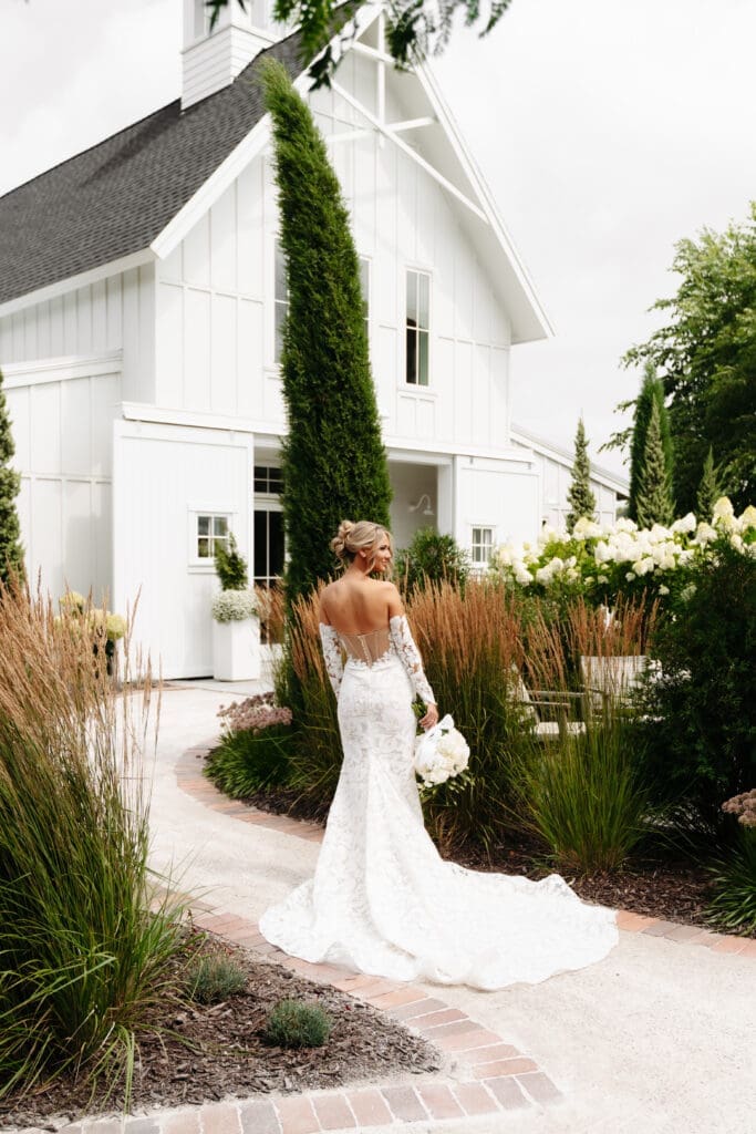 Bride walking through the gardens outside the white barn surrounded by hydrangeas and ornamental grasses.