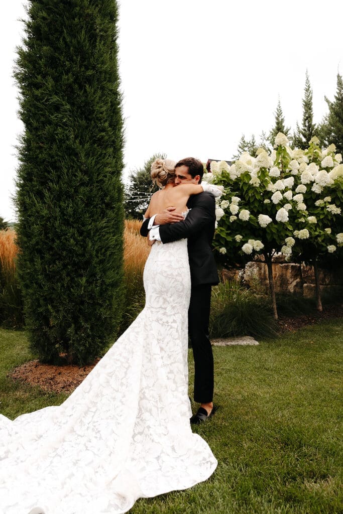 Emotional embrace during a wedding first look in a Minnesota garden with lush white hydrangeas at Redeemed Farm.