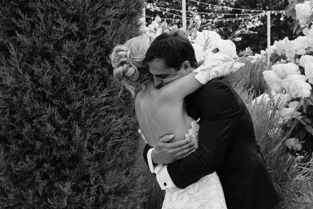 Bride and groom embrace during an emotional first look surrounded by garden florals, a favorite moment captured through wedding photography and videography packages.
