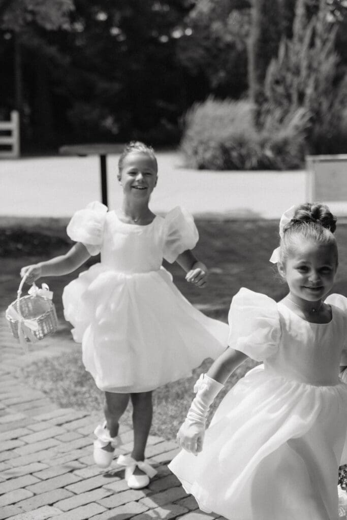 Flower girls in matching white dresses running across the courtyard of estate wedding venue with their baskets.
