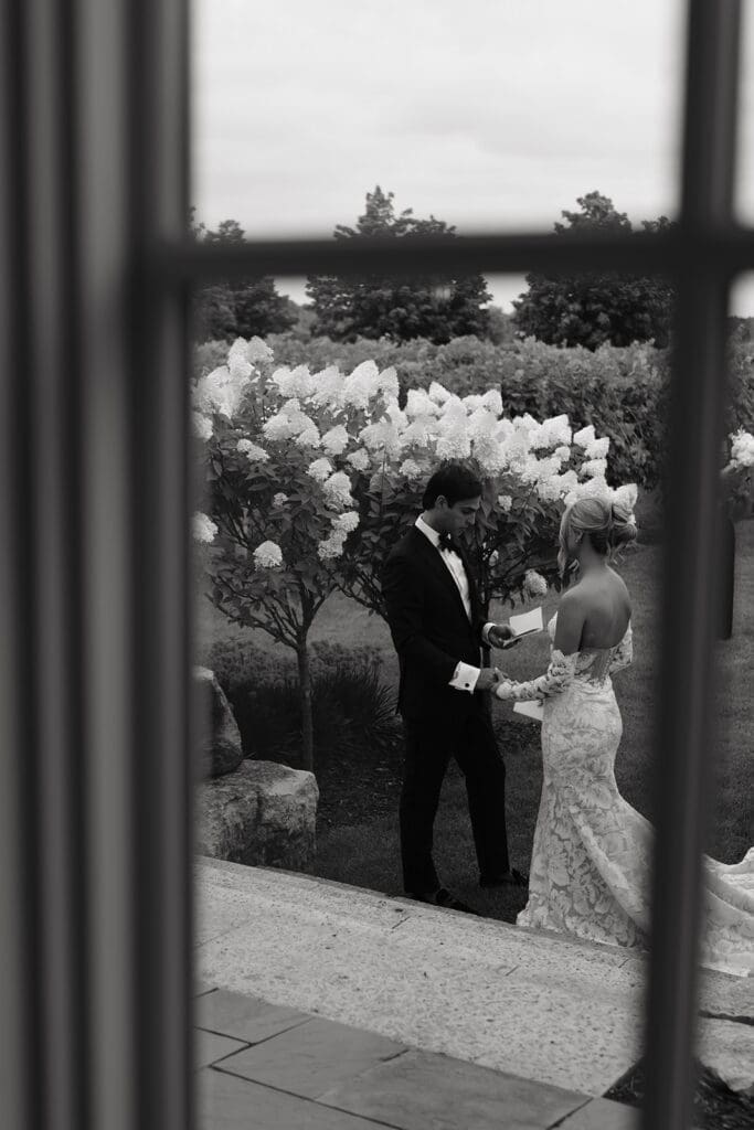 Bride and groom share private vows during their wedding first look at Redeemed Farm, framed through a window by a Minnesota wedding photographer.
