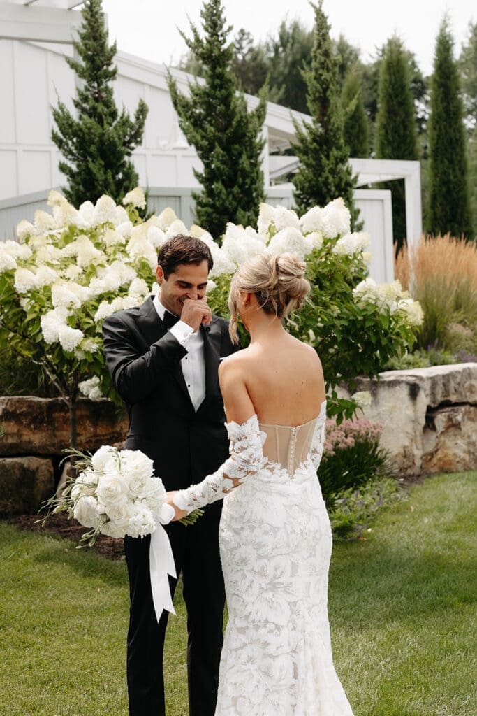 Groom wipes away tears during a heartfelt wedding first look surrounded by blooming hydrangeas.