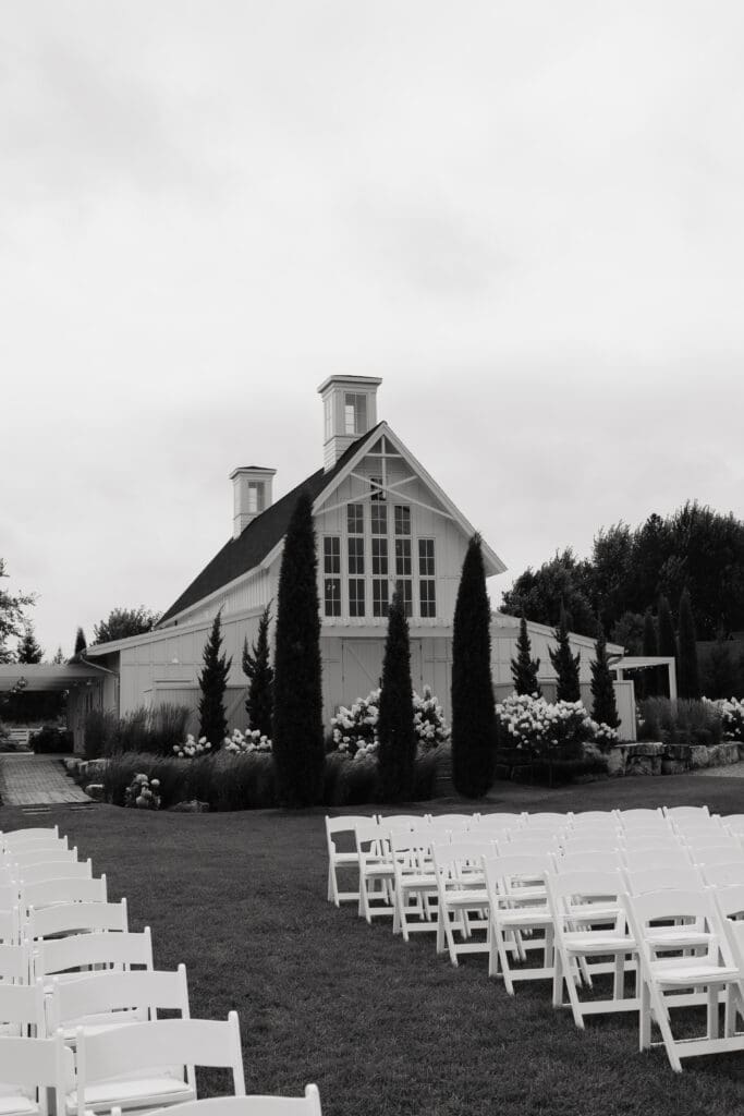 Outdoor ceremony setup with white folding chairs leading toward the white barn at Redeemed Farm MN.