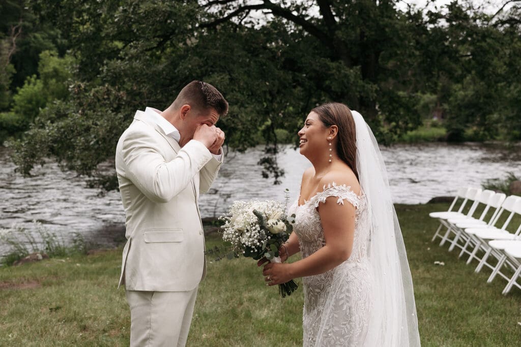 Groom wiping away tears during an emotional first look beside the river at La Pointe Events.