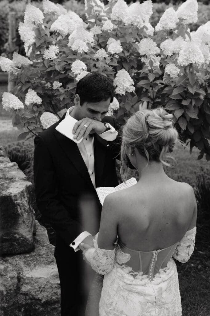 Groom getting extremely emotional as bride reads her vows to him in hydrangea-surrounded courtyard at Redeemed Farm in Scandia, MN.
