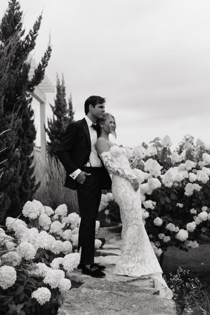 Bride and groom standing together among overflowing white hydrangeas and manicured gardens at Redeemed Farm MN, a luxury estate wedding venue in Scandia.
