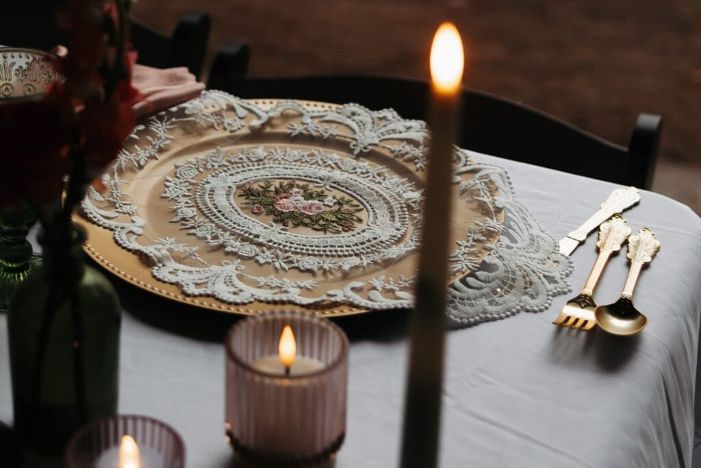 Vintage-inspired place setting with embroidered charger, candlelight, and gold flatware, demonstrating how reception details contribute to wedding storytelling.