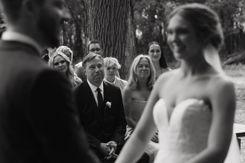 Guests watch the couple exchange vows during an intimate forest wedding ceremony, showcasing emotional reactions that elevate wedding photography and videography packages.