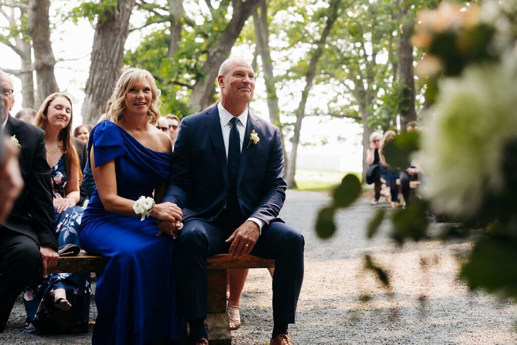 Parents of the groom beam up at the couple as they exchange vows during their intimate outdoor wedding ceremony in Minnesota.