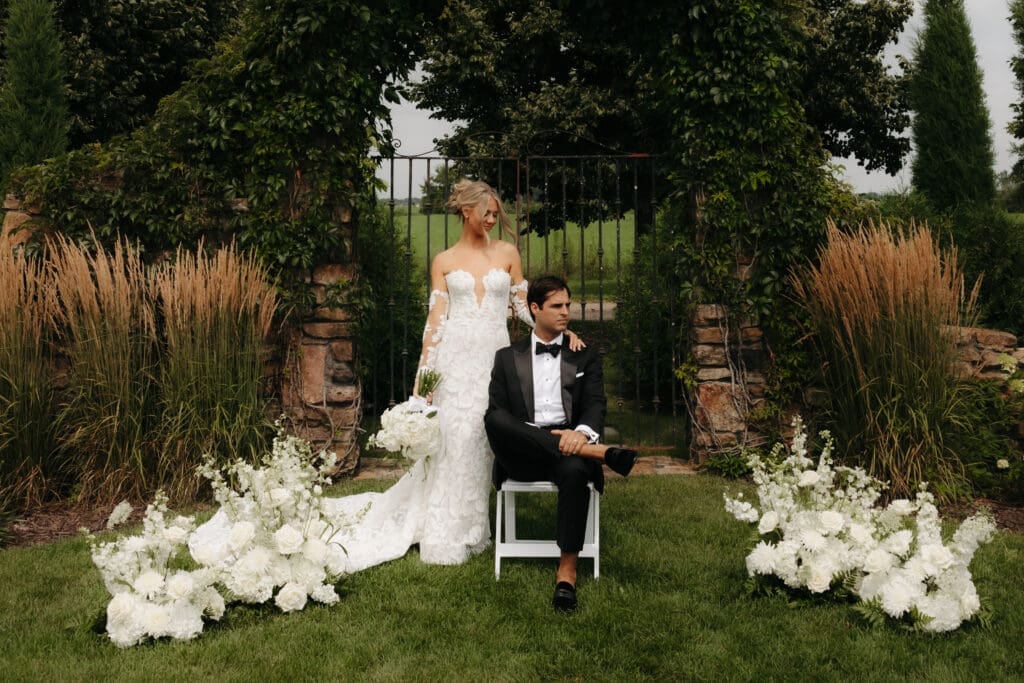 Editorial-style wedding portrait featuring a bride and groom surrounded by white florals and garden greenery.