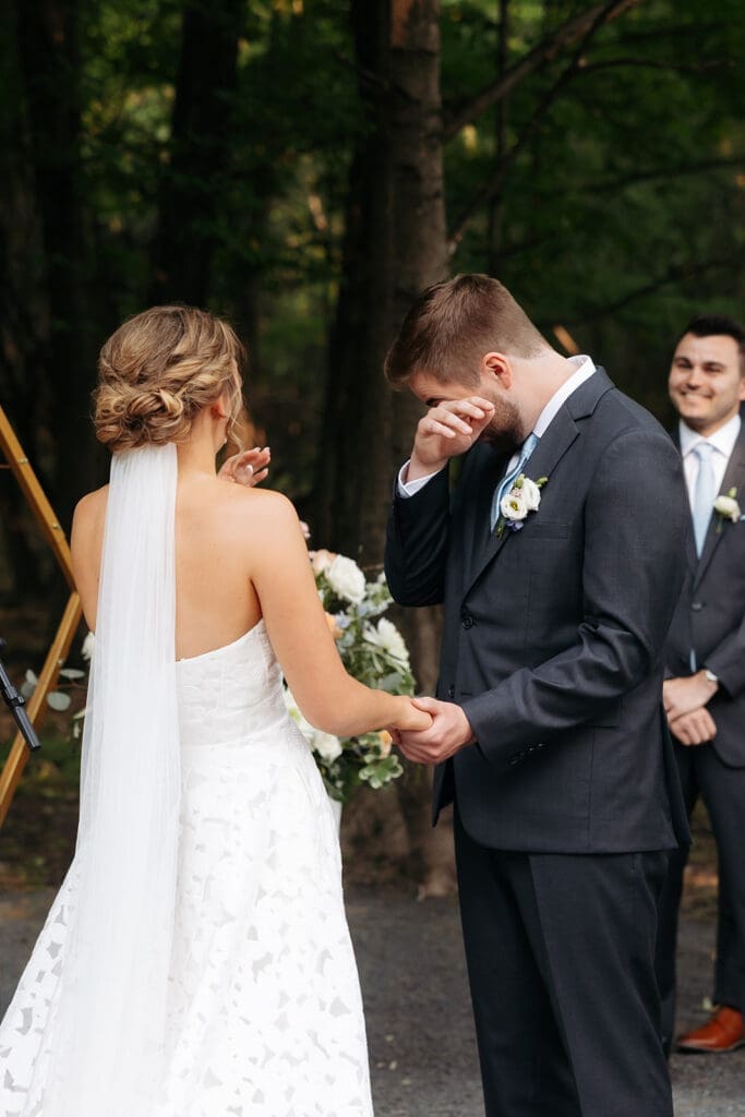 Groom wiping away tears as he sees his bride during their outdoor ceremony at a romantic luxury wedding venue in Minnesota.