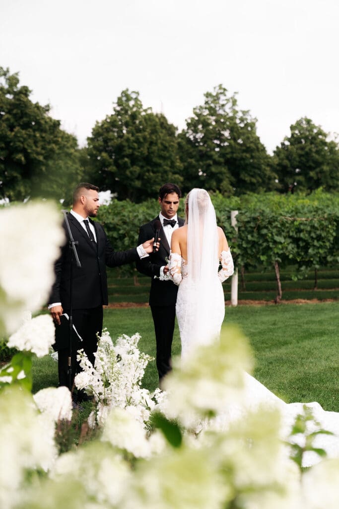 Bride and groom stand at the altar during an outdoor wedding ceremony surrounded by lush florals and vineyard views, creating a scene of maximum romance.