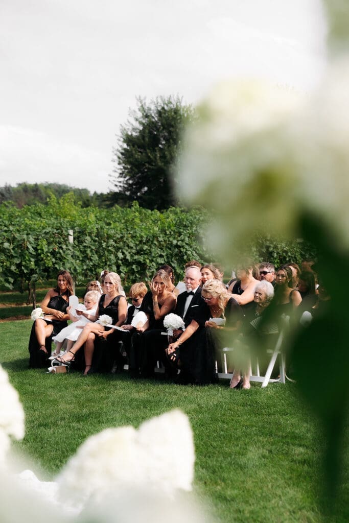 Wedding guests react during an outdoor ceremony while framed by soft florals in the foreground, one of the wedding photo tips that adds depth and storytelling to ceremony imagery.