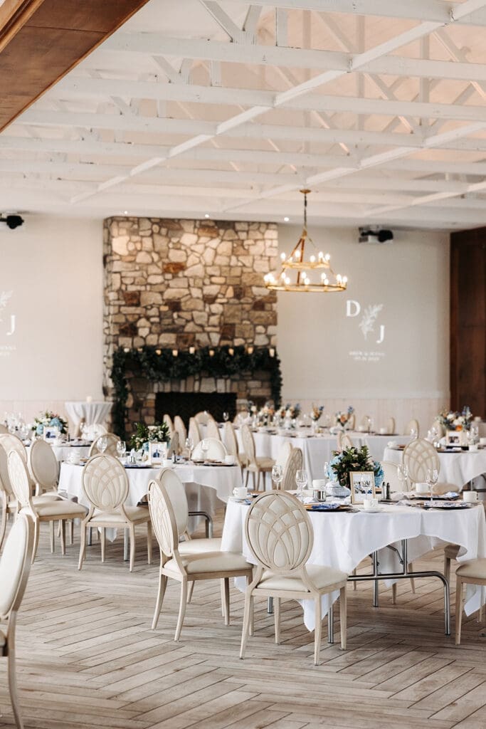 Bright reception space inside Equestria West at Bavaria Downs featuring white walls, exposed beams, and a stone fireplace at a luxury wedding venue.