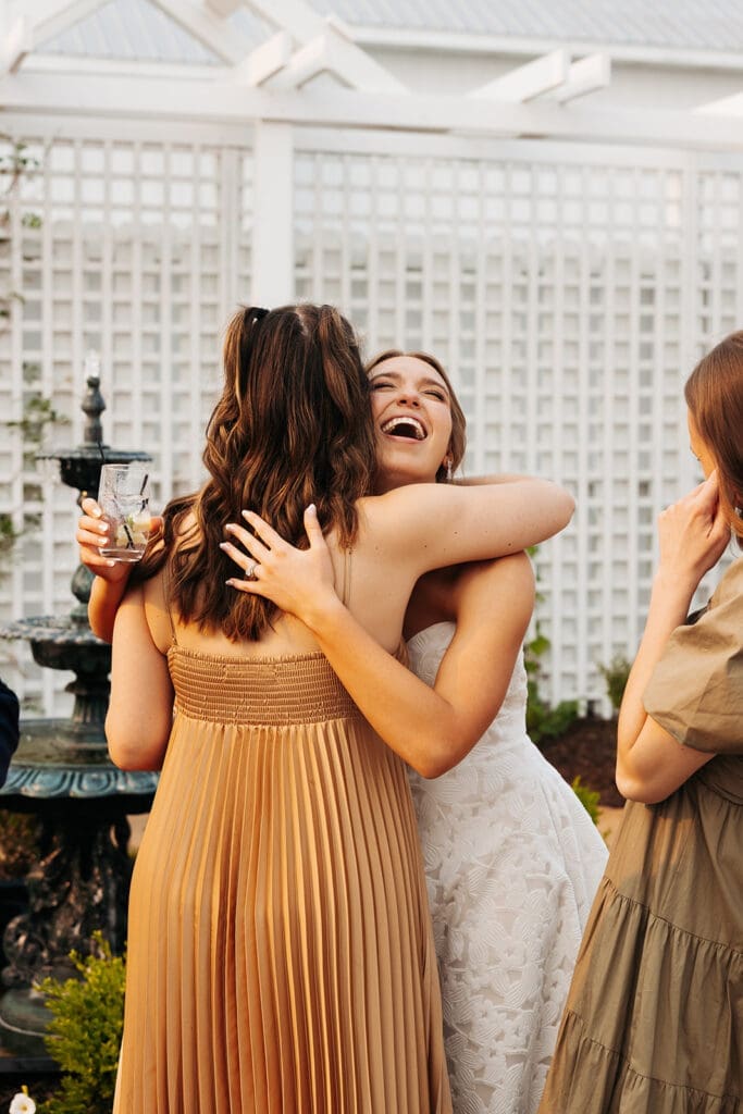 Bride hugs a friend during cocktail hour after enjoying a wedding day timeline with a first look.