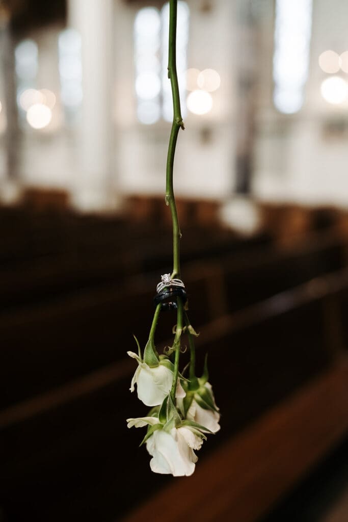 Single white floral stem suspended above church pews, creating a minimalist shot with soft bokeh in the background.