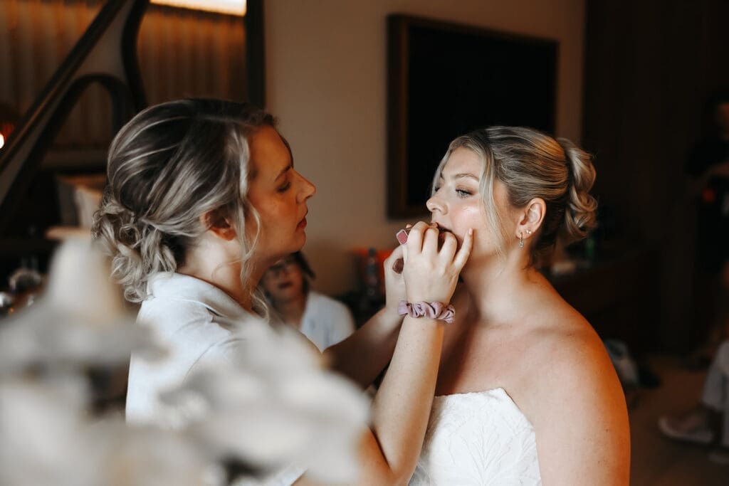 Bride stands calmly while mother of the bride helps her put on lipstick.