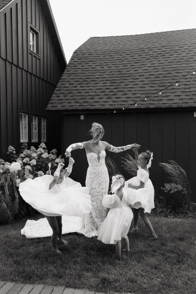 Bride twirling with flower girls outside the barn during portraits at vineyard wedding venue.