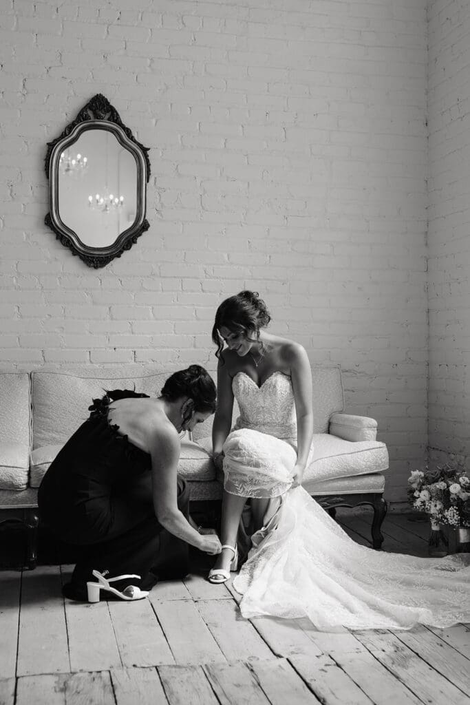 Bridesmaid helps adjust the bride's gown during final preparations, highlighting the meaningful behind-the-scenes moments of a wedding day.