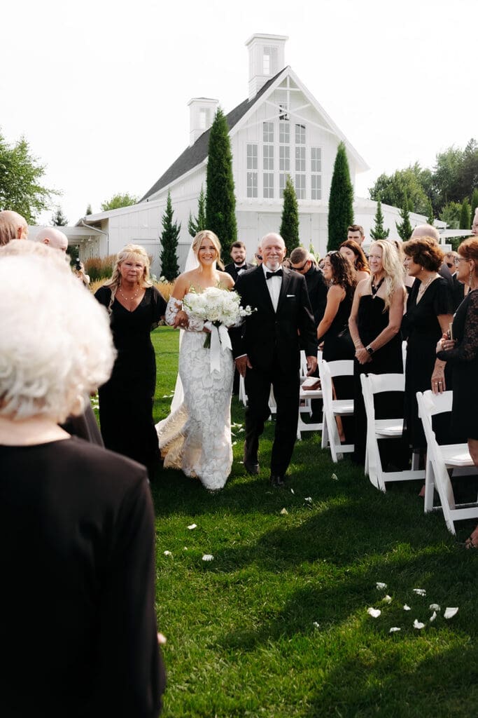 Bride and her father walk through a long ceremony aisle toward the altar at a garden wedding, a perfect example of how ceremony layout impacts wedding photography and videography packages.