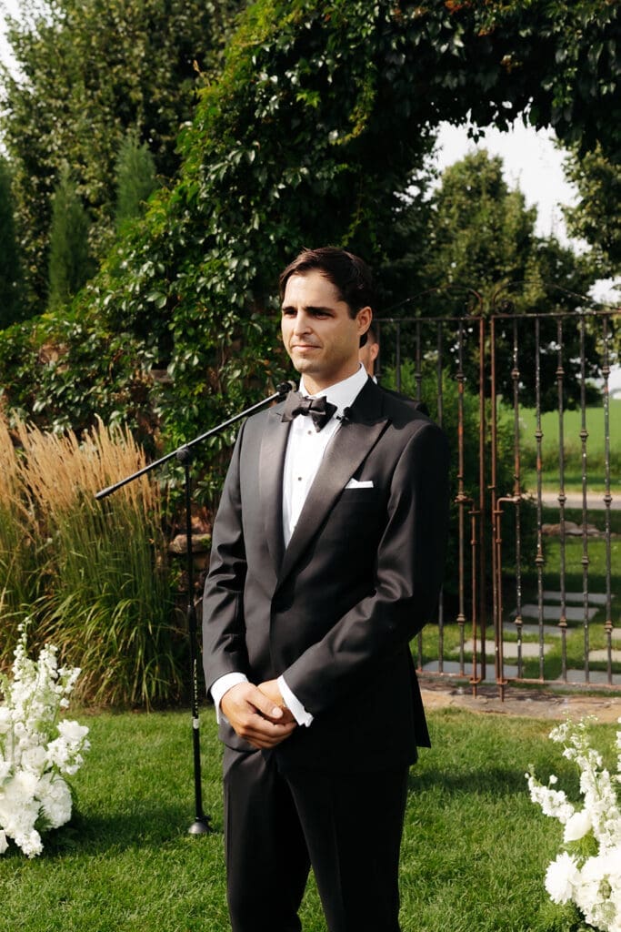 Groom waits at the ceremony altar moments before seeing his bride, creating anticipation and maximum romance during an outdoor wedding ceremony.