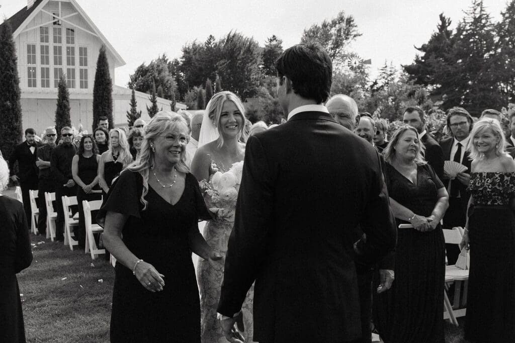 Bride reaches the altar and smiles at her groom as family members react around them during an emotional outdoor wedding ceremony.