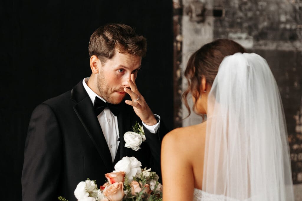 Groom wipes away tears after seeing his bride during their wedding first look.