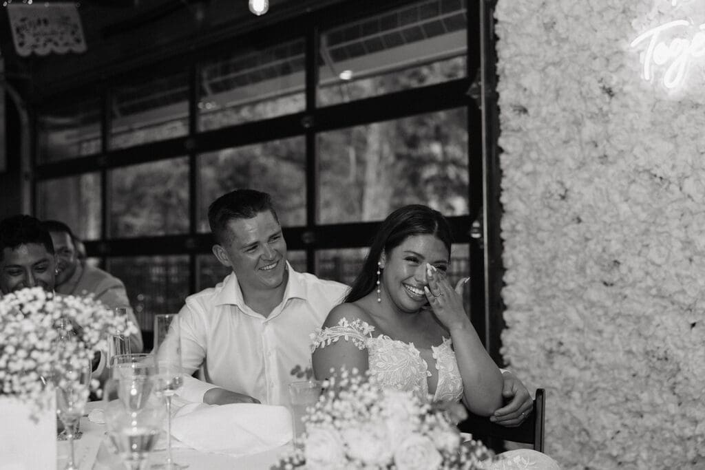 Newlyweds laughing during heartfelt reception speeches inside this elegant luxury wedding venue.