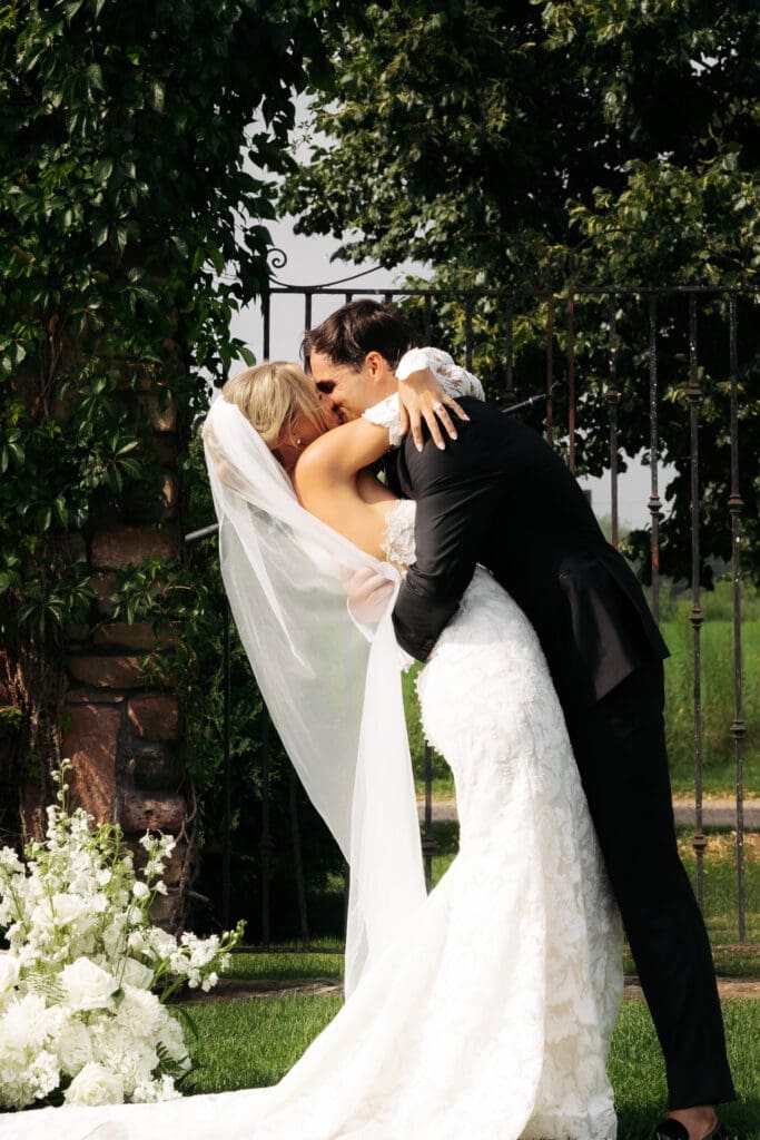 Bride and groom embracing beside a lush white floral installation during portraits at Redeemed Farm MN.