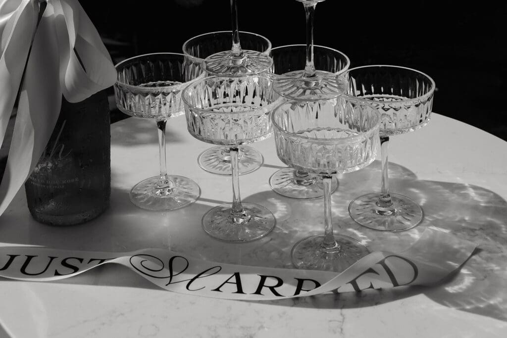 Vintage coupe glasses gathered on a marble surface beside a custom "Just Married" ribbon.