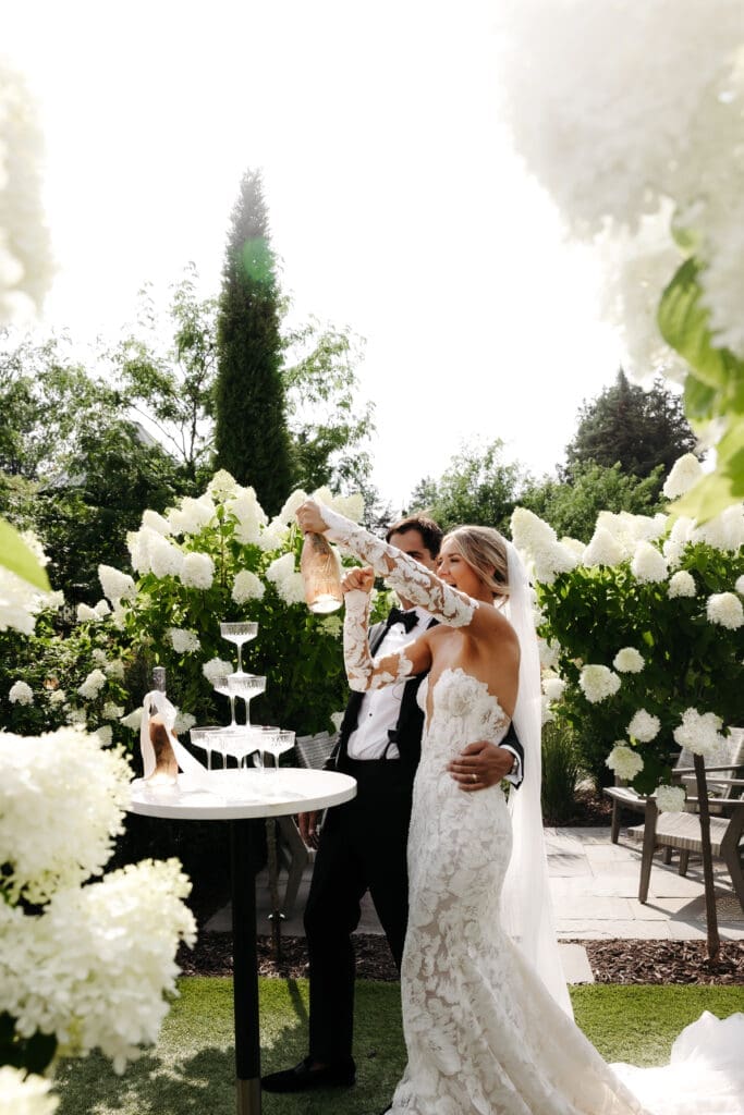 Bride and groom pouring champagne into a champagne tower surrounded by hydrangeas and garden blooms at Minnesota estate wedding venue.