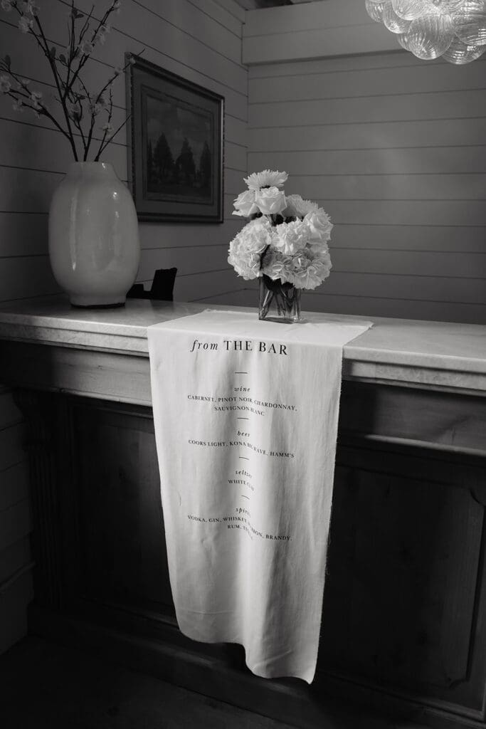Custom cocktail menu displayed on linen draping over a reception bar, photographed as a personalized wedding detail.