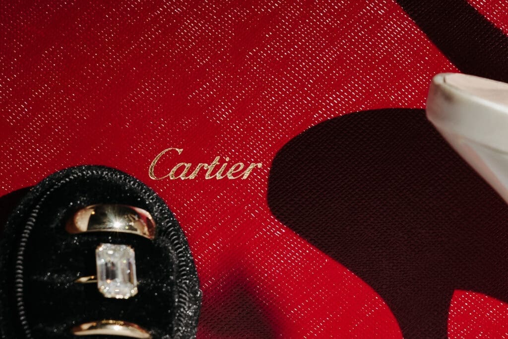 Close-up featuring wedding bands and an emerald-cut engagement ring beside a Cartier ring box.